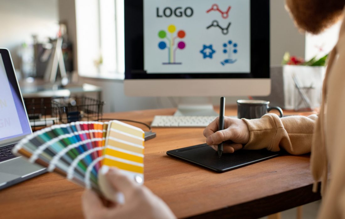 Hands of creative male freelance designer choosing colors from palette and using touchpad and stylus while drawing logo on computer screen